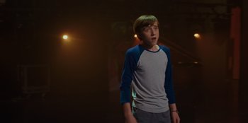 Movie still from “Better Nate Than Ever” (2022), directed by Tim Federle – A young man standing in a dark room; Medium shot, Over the shoulder angle