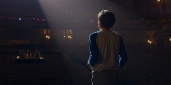 Movie still from “Better Nate Than Ever” (2022), directed by Tim Federle – A young boy standing in front of an audience at a theater; Wide shot, Over the shoulder angle