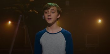 Movie still from “Better Nate Than Ever” (2022), directed by Tim Federle – A young man in a blue and white shirt is singing; Medium shot, Over the shoulder angle