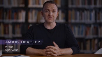 Movie still from “Beyond Infinity: Buzz and the Journey to Lightyear” (2022), directed by Tony Kaplan – A man sitting at a table in front of bookshelves; Medium shot, High angle