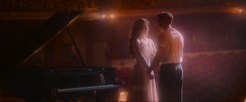 A man and a woman holding hands in front of a grand piano