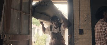 Movie still from “Big George Foreman” (2023), directed by George Tillman Jr. – A man in overalls is holding a pillow over his head; Medium shot, High angle