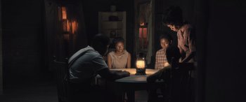Movie still from “Big George Foreman” (2023), directed by George Tillman Jr. – A group of people sitting around a table in the dark; Medium shot, High angle