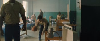 Movie still from “Big George Foreman” (2023), directed by George Tillman Jr. – A group of men playing a game of basketball in a dorm room; Wide shot, High angle