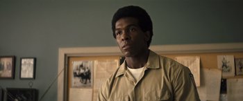 Movie still from “Big George Foreman” (2023), directed by George Tillman Jr. – A man in a tan shirt is standing in front of a picture; Close Up shot, Low angle