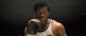 Movie still from “Big George Foreman” (2023), directed by George Tillman Jr. – A man wearing a boxing glove in front of a black background; Close Up shot, Low angle