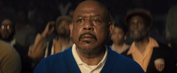 Movie still from “Big George Foreman” (2023), directed by George Tillman Jr. – An older man with a beard and mustache wearing a blue sweater; Close Up shot, Low angle