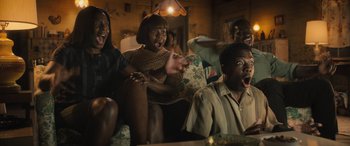 Movie still from “Big George Foreman” (2023), directed by George Tillman Jr. – A group of people sitting on a couch watching television; Medium shot, High angle