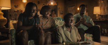 Movie still from “Big George Foreman” (2023), directed by George Tillman Jr. – A group of people sitting on top of a wooden table; Medium shot, High angle