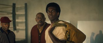 Movie still from “Big George Foreman” (2023), directed by George Tillman Jr. – A man standing next to another man holding a backpack; Medium shot, Low angle