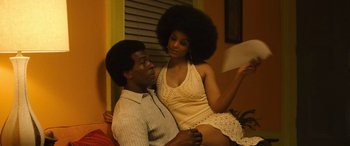 Movie still from “Big George Foreman” (2023), directed by George Tillman Jr. – A man and a woman sitting next to each other on a couch; Medium shot, Low angle