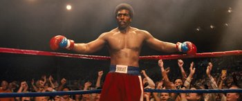 Movie still from “Big George Foreman” (2023), directed by George Tillman Jr. – A man standing in a boxing ring with his hands in the air; Medium shot, Low angle