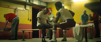 Movie still from “Big George Foreman” (2023), directed by George Tillman Jr. – Two men sitting on a bench in front of another man; Medium shot, Low angle