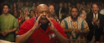 Movie still from “Big George Foreman” (2023), directed by George Tillman Jr. – An older man in a red shirt is holding his hands to his mouth; Close Up shot, Low angle