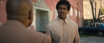 Movie still from “Big George Foreman” (2023), directed by George Tillman Jr. – A man in a brown shirt and a man in a tan shirt looking to his left; Medium shot, Low angle