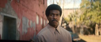 Movie still from “Big George Foreman” (2023), directed by George Tillman Jr. – A man in a brown shirt and a pink building; Close Up shot, Low angle