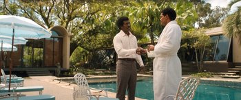 Movie still from “Big George Foreman” (2023), directed by George Tillman Jr. – Two men standing next to each other in front of a swimming pool; Medium shot, Over the shoulder angle