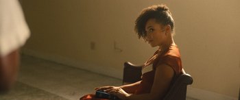 Movie still from “Big George Foreman” (2023), directed by George Tillman Jr. – A woman sitting in a chair with a book in her lap; Medium shot, Over the shoulder angle