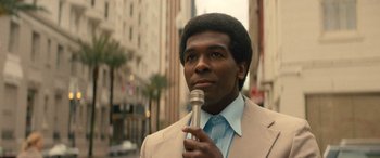 Movie still from “Big George Foreman” (2023), directed by George Tillman Jr. – A man holding a microphone while standing on the street; Close Up shot, Low angle