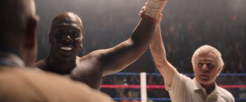 Movie still from “Big George Foreman” (2023), directed by George Tillman Jr. – A man in a boxing ring holding his hands up in the air; Close Up shot, Low angle