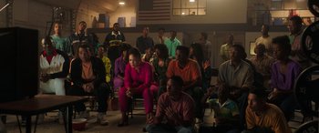 Movie still from “Big George Foreman” (2023), directed by George Tillman Jr. – A group of people sitting and standing in a room; Wide shot, High angle