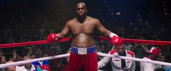 Movie still from “Big George Foreman” (2023), directed by George Tillman Jr. – A man in red and white trunks stands in a boxing ring; Medium shot, Low angle