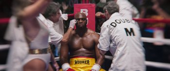 Movie still from “Big George Foreman” (2023), directed by George Tillman Jr. – A man in a boxing ring getting ready for a fight; Medium shot, High angle