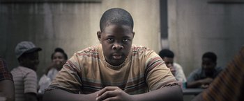 Movie still from “Big George Foreman” (2023), directed by George Tillman Jr. – A young man sitting in front of a wall; Close Up shot, Low angle