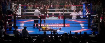 Movie still from “Big George Foreman” (2023), directed by George Tillman Jr. – A man laying on the ground in a boxing ring; Extreme Wide shot, Overhead angle