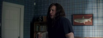 Movie still from “Big Gold Brick” (2022), directed by Brian Petsos – A man with long brown hair holding a nintendo wii game controller; Medium shot, Over the shoulder angle
