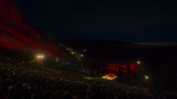 Movie still from “Bill Burr: Live at Red Rocks” (2022), directed by Mike Binder – A crowd of people sitting on a stage at night; Extreme Wide shot, High angle