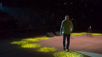 Movie still from “Bill Burr: Live at Red Rocks” (2022), directed by Mike Binder – A man standing on a stage while holding a microphone; Extreme Wide shot, Low angle