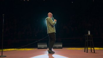 Movie still from “Bill Burr: Live at Red Rocks” (2022), directed by Mike Binder – A man standing on a stage holding a microphone; Wide shot, Low angle