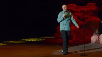Movie still from “Bill Burr: Live at Red Rocks” (2022), directed by Mike Binder – A man standing on a stage holding a microphone; Wide shot, High angle