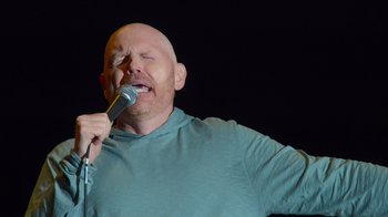 Movie still from “Bill Burr: Live at Red Rocks” (2022), directed by Mike Binder – A bald man is singing into a microphone; Close Up shot, Low angle