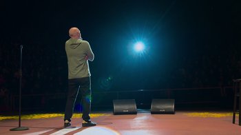 Movie still from “Bill Burr: Live at Red Rocks” (2022), directed by Mike Binder – A man standing in front of two speakers on a stage; Medium shot, Low angle
