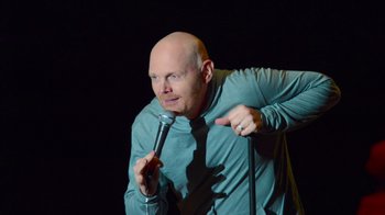 Movie still from “Bill Burr: Live at Red Rocks” (2022), directed by Mike Binder – A bald man holding a microphone in front of a black background; Medium shot, High angle