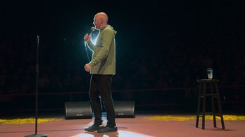 Movie still from “Bill Burr: Live at Red Rocks” (2022), directed by Mike Binder – A man standing on a stage holding a microphone; Medium shot, Low angle