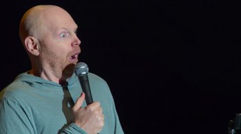 Movie still from “Bill Burr: Live at Red Rocks” (2022), directed by Mike Binder – A bald man is holding a microphone up to his mouth; Close Up shot, Over the shoulder angle