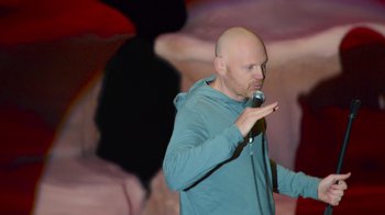 Movie still from “Bill Burr: Live at Red Rocks” (2022), directed by Mike Binder – A bald man in a blue shirt is holding a microphone; Medium shot, Low angle