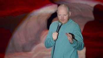 Movie still from “Bill Burr: Live at Red Rocks” (2022), directed by Mike Binder – A bald man holding a microphone while standing on a stage; Medium shot, High angle