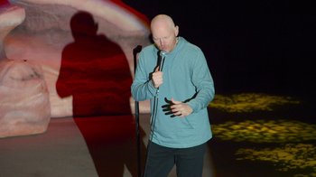 Movie still from “Bill Burr: Live at Red Rocks” (2022), directed by Mike Binder – A man standing on a stage holding a microphone; Medium shot, High angle