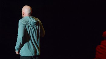Movie still from “Bill Burr: Live at Red Rocks” (2022), directed by Mike Binder – A bald headed man wearing a blue shirt and black pants; Medium shot, Over the shoulder angle
