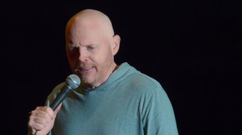 Movie still from “Bill Burr: Live at Red Rocks” (2022), directed by Mike Binder – A bald man is holding a microphone up to his face; Close Up shot, Over the shoulder angle