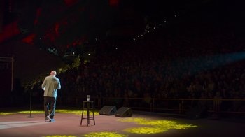 Movie still from “Bill Burr: Live at Red Rocks” (2022), directed by Mike Binder – A man standing on a stage in front of an audience; Extreme Wide shot, High angle