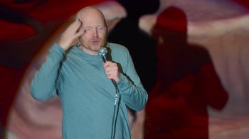 Movie still from “Bill Burr: Live at Red Rocks” (2022), directed by Mike Binder – A bald man holding a microphone in front of his face; Medium shot, Over the shoulder angle