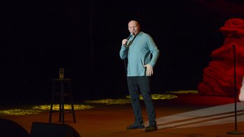 Movie still from “Bill Burr: Live at Red Rocks” (2022), directed by Mike Binder – A man standing on a stage holding a microphone; Medium shot, High angle