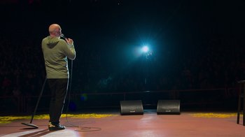 Movie still from “Bill Burr: Live at Red Rocks” (2022), directed by Mike Binder – A man standing on a stage holding a microphone; Wide shot, Low angle