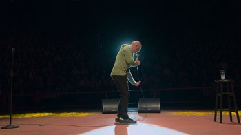 Movie still from “Bill Burr: Live at Red Rocks” (2022), directed by Mike Binder – A man standing on a stage holding a microphone; Wide shot, High angle