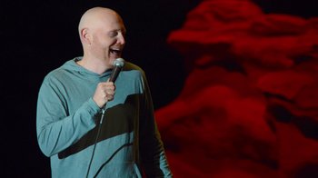 Movie still from “Bill Burr: Live at Red Rocks” (2022), directed by Mike Binder – A bald man with a shaved head holding a microphone; Medium shot, High angle